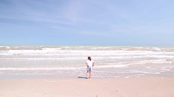 Menina caminha ao longo da praia em setembro. Céu azul oceano, ondas e uma criança em roupas de verão. — Vídeo de Stock
