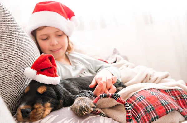 Mała świąteczna dziewczynka i cocker spaniel szczeniak. Szczęśliwe dziecko w kapeluszu Mikołaja trzyma psa w rękach — Zdjęcie stockowe