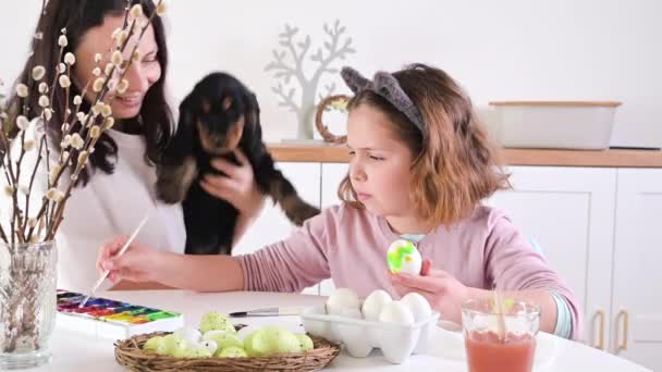 Mała dziewczynka, mama i jej szczeniaczek malują jajka na Wielkanoc. — Wideo stockowe