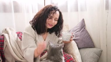 Esmer kadın kanepede kahve içiyor. Bir bayan sabahları bir fincan çay ya da kahveyle rahat bir evin parlak odasında dinleniyor. Oral zamanda bilinçli rahatlama