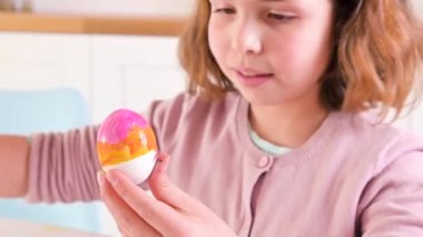 Küçük bir kız Paskalya için yumurta boyuyor. Avrupa görünümlü çocuk okul çocuğu ve masada paskalya yumurtası, dekor. Işıl ışıl ve doğal çekim.