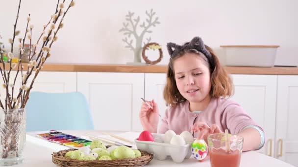 小さな女の子がイースターのために卵を描きます ヨーロッパの外観とイースターエッグの子供の学童は テーブルの上に装飾 光のインテリアと自然なショット コピースペース 高品質4K映像 — ストック動画