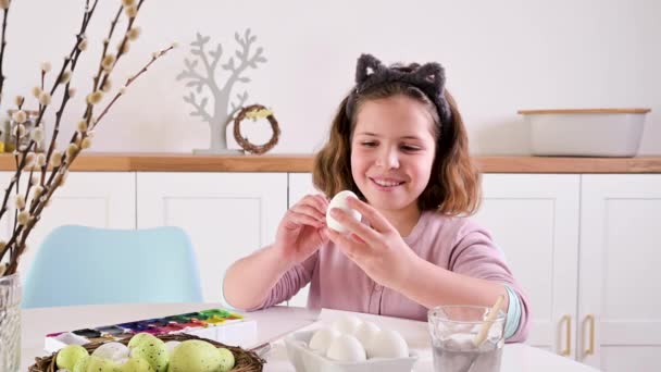 小さな女の子がイースターのために卵を描きます ヨーロッパの外観とイースターエッグの子供の学童は テーブルの上に装飾 光のインテリアと自然なショット コピースペース 高品質4K映像 — ストック動画