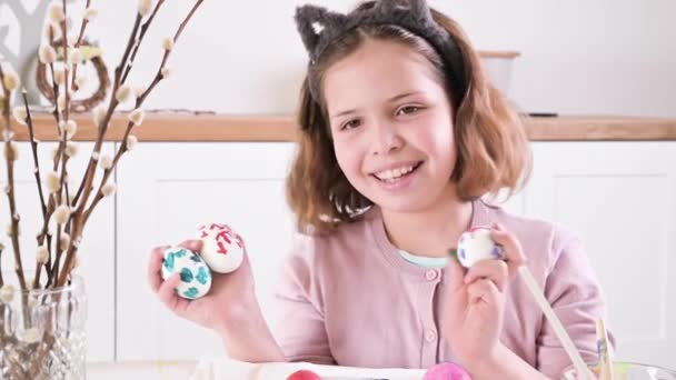 Holčička maluje vajíčka na Velikonoce. Dítě školák evropského vzhledu a velikonoční vajíčka, dekor na stole. Světlý interiér a přirozené záběry. — Stock video