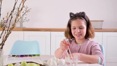 Küçük bir kız Paskalya için yumurta boyuyor. Avrupa görünümlü çocuk okul çocuğu ve masada paskalya yumurtası, dekor. Işıl ışıl ve doğal çekim.