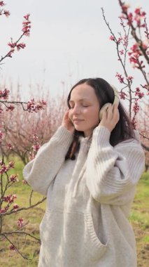 Genç bir kadın kulaklıkla müzik dinler ve meditasyon yapar, baharda çiçek açan bir bahçede olur. Harika bir rahatlama ve sükunet anı. Doğayla barış ve birlik.