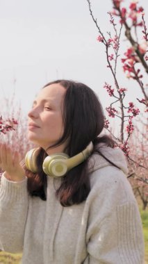 Genç bir kadın kulaklıkla müzik dinler ve meditasyon yapar, baharda çiçek açan bir bahçede olur. Harika bir rahatlama ve sükunet anı. Doğayla barış ve birlik.