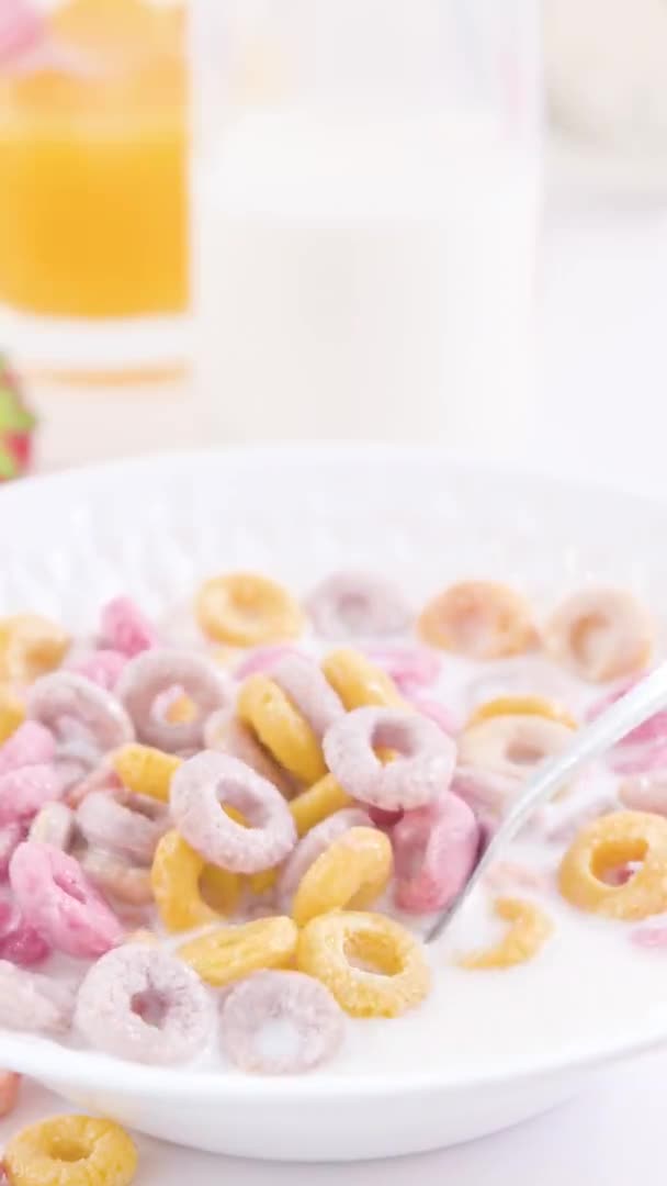 Desayuno seco en un tazón con leche. Anillos multicolores para el desayuno de los niños. Formato vertical, para smartphones y redes sociales. Primer plano de la comida en una cuchara. — Vídeo de stock