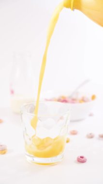 Bir bardak portakal suyu. Meyve suyu arka plandaki bir bardağa dökülür. Vitamin kahvaltısı ve sağlıklı. Yanında bir kase mısır gevreği var. Ağır çekim. görüntüler