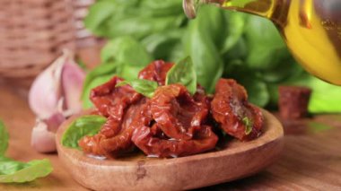 Zeytinyağında kurutulmuş domates, kasenin yanında fesleğen. Yağ sızdırıyor. Geleneksel İtalyan ve İspanyol aperatifleri aperatif ve tost için. Yakın plan. 4K görüntü. Ahşap bir arka plana yakın plan. stilsel kırsal