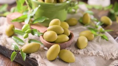 Large green olives in a cup on a wooden table. Italian olives, Sardenya and Greece harvest. High quality FullHD footage. Falling berries on the table