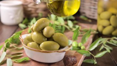 Large green olives in a cup on a wooden table. Italian olives, Sardenya and Greece harvest. Olive oil is poured on the berries, olive leaves in the frame. close-up