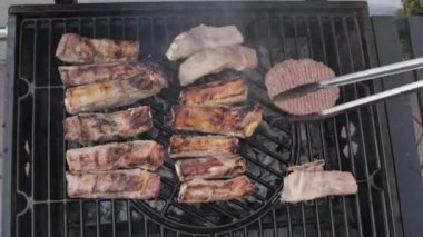 Grilled meat. Pork ribs on fire. Barbecue in the open space. Man turns over pieces of meat and smoke. View from above. High quality 4k footage