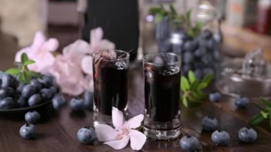 Mirto liqueur. A traditional blueberry liqueur from Sardinia, Italy. Sweet and aromatic drink at the end of the meal. Two small glasses with an alcoholic drink on the table and blueberries. slowmotion