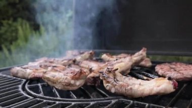 Grilled meat. Pork ribs on fire. Barbecue in the open space. Man turns over pieces of meat and smoke. Grill lid movement closes