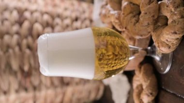 Pouring beer into the glass. Wheat spikelets with one mugs of beer on wooden background. Cold lager beer. Craft beer forms waves. Freshness and foam.Nearby are Neapolitan taralli from Italy. vertical