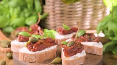 Bruschetta with sun-dried tomatoes, cheese, basil and capers. Traditional appetizer for aperitivo in Italy. Pouring olive oil on toast. High quality photo. Copy space