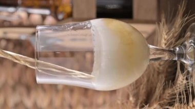 A glass of light craft beer on a wooden table. Beer is poured into a glass with foam and bubbles. Vertical video for social media or advertising. beer texture. 4k footage