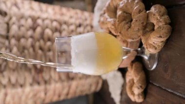 Pouring beer into the glass. Wheat spikelets with one mugs of beer on wooden background. Cold lager beer. Craft beer forms waves. Freshness and foam.Nearby are Neapolitan taralli from Italy. vertical