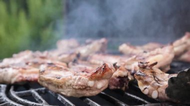 Grilled meat. Pork ribs on fire. Barbecue in the open space. Man turns over pieces of meat and smoke. Grill lid movement closes