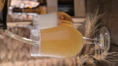A glass of light craft beer on a wooden table. Beer is poured into a glass with foam and bubbles. Vertical video for social media or advertising. beer texture. footage