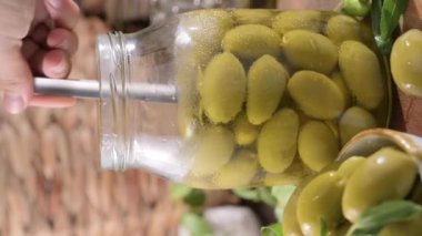 Large green olives in a cup on a wooden table. Italian olives, Sardenya and Greece harvest, olive leaves in the frame. close-up. Olive berries in a large jar and stacked separately. Vertical video
