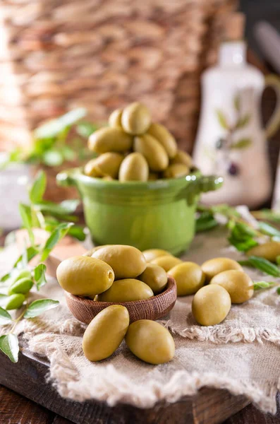 Large green olives in a cup on a wooden table. Italian olives, Sardenya and Greece harvest. Olive oil is poured on the berries, olive leaves in the frame. close-up. Copy sapce