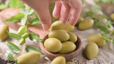 Large green olives in a cup on a wooden table. Italian olives, Sardenya and Greece harvest. Olive oil is poured on the berries, olive leaves in the frame. close-up