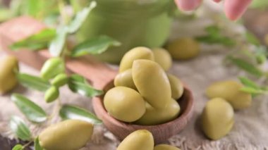Large green olives in a cup on a wooden table. Italian olives, Sardenya and Greece harvest. Olive oil is poured on the berries, olive leaves in the frame. close-up