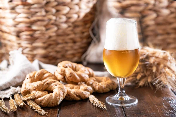 Pouring beer into the glass. Wheat spikelets with one mugs of beer on wooden background. Cold lager beer. Craft beer forms waves. Freshness and foam.Nearby are Neapolitan taralli from Italy