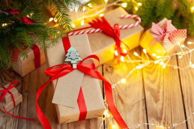Noel farklı hediye kutuları bir noel ağacının altındaki ahşap masada. El yapımı gelenekler kırmızı kurdele ve dekorasyon sanatıyla sunuluyor. Mutlu yeni yıl kutlamaları..