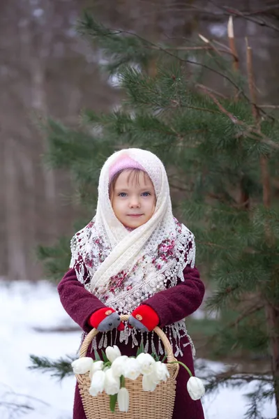 在冬季的森林里 一个可爱的小女孩提着一篮子白郁金香 免版税图库图片