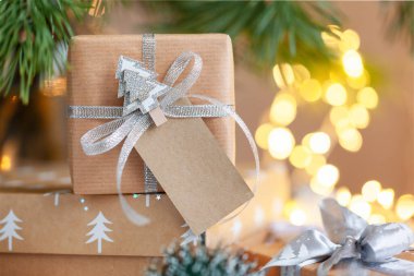 Noel hediyesi kutusu, köknar ağacının altındaki adres kartı etiketi ile süslenmiş, arka planda odanmamış ışıklar var. Noel ve Yeni Yıl kavramı.