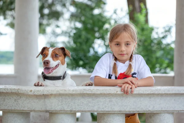 Portrait little blonde girl child and Jack Russell Terrier dog in nature. A special bond between the kid and its dog. Love and affection.