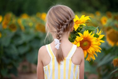 Hasır şapkalı, ayçiçeği tarlasının arka planında bir buket ayçiçeği olan küçük sarışın kız. Arka plan.