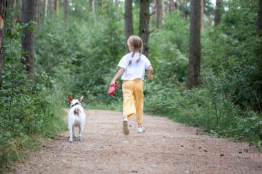 Orman yaz gününde köpekli tasasız bir çocuk yürüyüş yolunda koşuyor. Evcil hayvanla koşan mutlu kız. Arka plan.