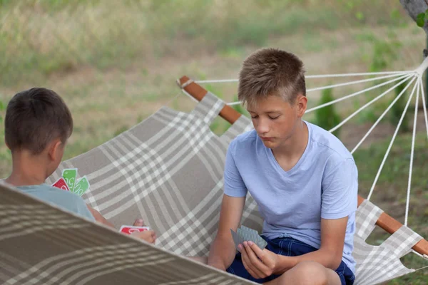 かわいい2人の男の子の兄弟は夏の日にハンモックに座ってボードゲームをしています 屋外でトランプをする子供たち — ストック写真