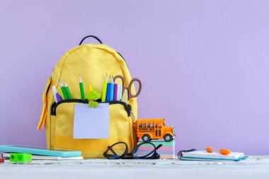 Okula dönüş kavramı. Tam sarı okul çantası ve mor arka planda kırtasiye malzemesi olan oyuncak otobüs okulu..