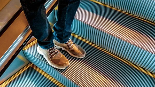 高角度透视拍摄了穿牛仔裤和运动鞋的男子越过台阶机械楼梯的细节 — 图库照片