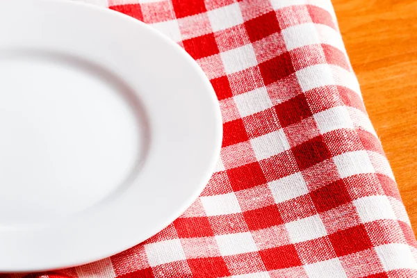 Empty white plate on a red and white tablecloth — Stock Photo, Image