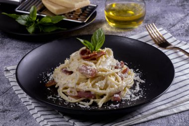 Carbonara usulü makarna. Pastırma, parsel ve parmesan peynirli spagetti. Siyah tabakta parmesanlı Carbonara makarnası. İtalyan yemeği..