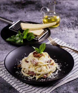 Carbonara usulü makarna. Pastırma, parsel ve parmesan peynirli spagetti. Siyah tabakta parmesanlı Carbonara makarnası. İtalyan yemeği..