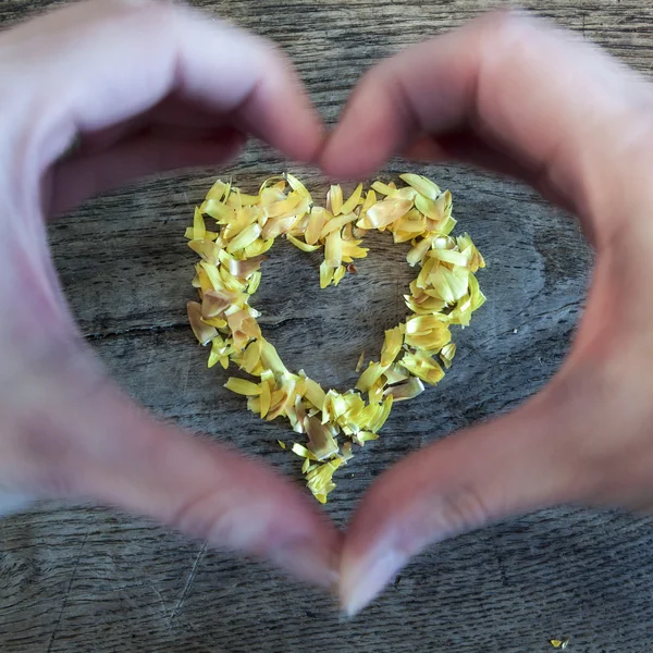 Ein Herz aus Blütenblättern, das auf einem Holztisch liegt und Hände — Stockfoto
