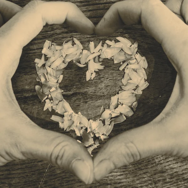 Un corazón de pétalos acostado en una mesa de madera y manos —  Fotos de Stock