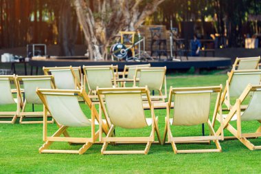 Çimenli masaları olan birçok boş beyaz iskemle gölgeli yeşil çimlerle çevrilidir. Bahçedeki teras sandalyelerinde rahat. Parktaki çim sandalyeleri. Bahçedeki güneş yatakları. Seçici odak.
