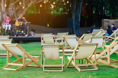 Bahçede akşam yemeği için masaları olan birçok beyaz iskemle arka planda müzikal performansın bulanık görüntüsüne sahip gölgeli yeşil çimlerle çevrilidir. Bahçedeki bahçe teras sandalyelerinde rahattır..