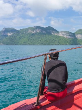 Siyah tişörtlü Asyalı adamın, balkonda rahatlarken, Samui adasının teknesinden manzaranın keyfini çıkarırken görüntüsü. Tropikal tatil beldelerinde mutlu erkek turistler. Gemi seyahatine çıkın..