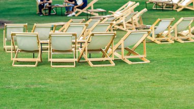 Çimenli masaları olan birçok boş beyaz iskemle gölgeli yeşil çimlerle çevrilidir. Bahçedeki teras sandalyelerinde rahat. Parktaki çim sandalyeleri. Bahçedeki güneş yatakları. Seçici odak.