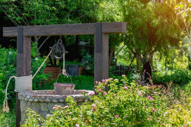 Taş ve tekerlek makara ile yapılmış güzel artezyen metal kova ve halatla huzurlu bahçe atmosferinde. Kırsal alandaki Retro Stone Kuyusu. Antika eşyalarla bahçe dekorasyonu.