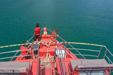 Erkek mürettebatın üst görüntüsü, adanın kıyısına demirlemeden önce geminin pruvasına şamandıra bağlamak için bir ip hazırladı. Dışarıda, tropikal tatil beldelerinde mutlu gündelik turizmler. Gemi seyahati.